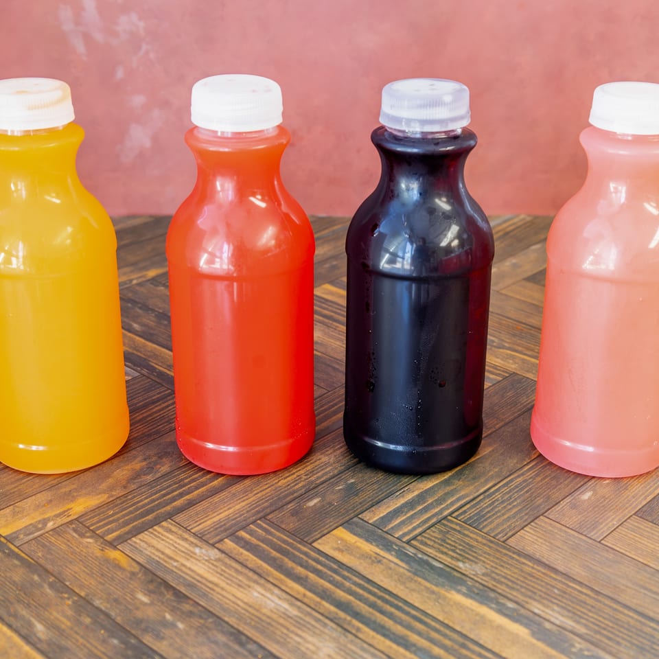 Assorted colorful juice bottles in yellow, red, black, and pink on a wooden table.