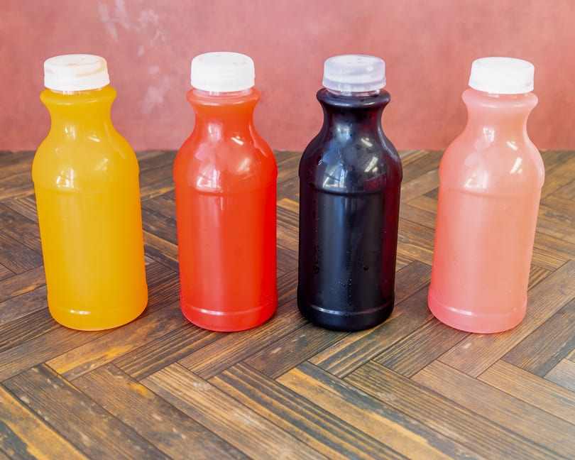 Assorted colorful juice bottles in yellow, red, black, and pink on a wooden table.