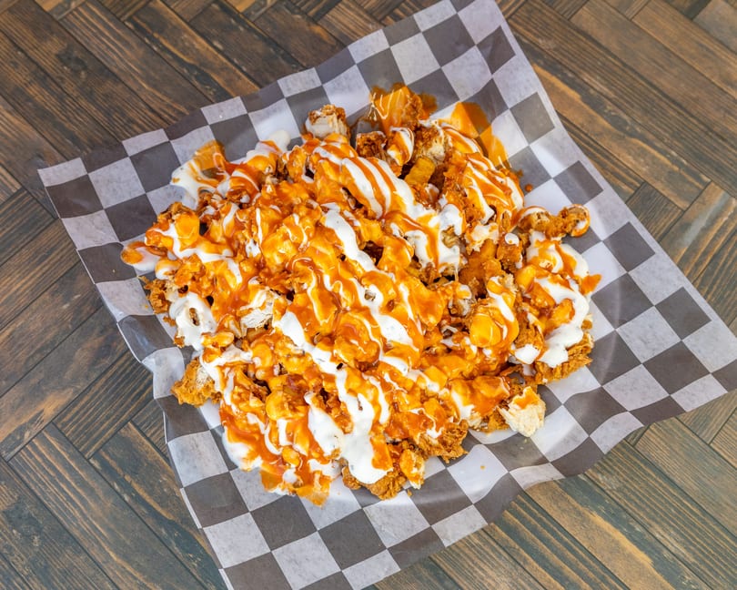 Loaded fried chicken pieces drizzled with orange buffalo and white ranch sauce on checkered paper.