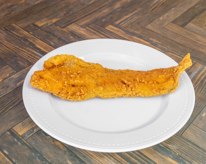 Crispy golden fried fish fillet served on a simple white plate.