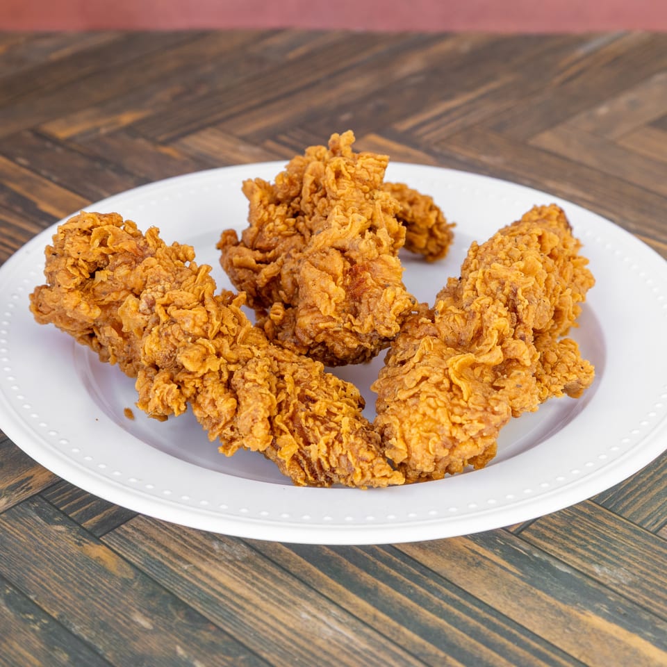Several golden-brown fried chicken tenders arranged on a white plate.