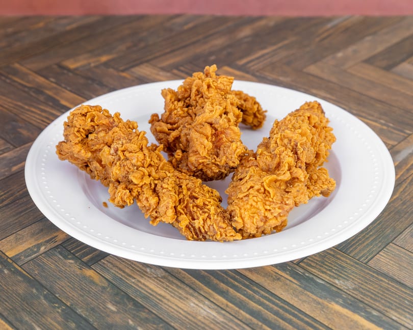 Several golden-brown fried chicken tenders arranged on a white plate.