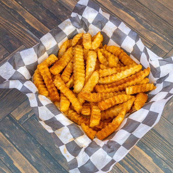 Seasoned crinkle-cut fries in a black and white checkered paper basket on a wooden table.