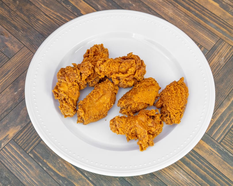 Golden-brown crispy fried chicken pieces on a white plate against a wooden table.