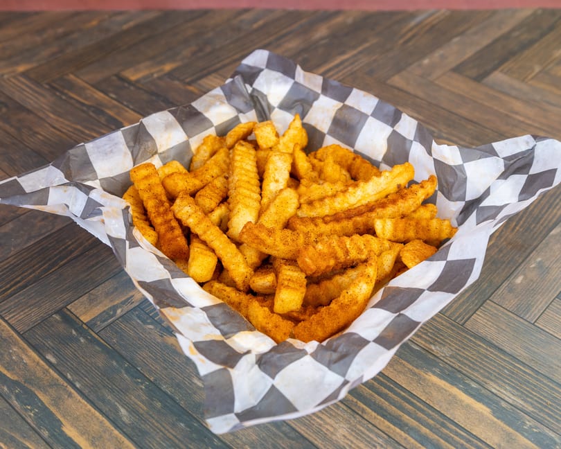 Golden seasoned crinkle-cut fries in a checkered paper basket on a wooden table.