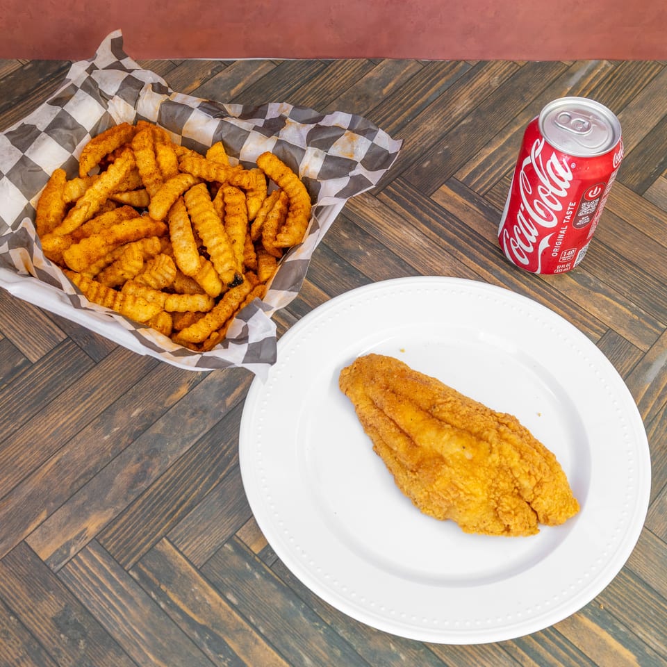 Fried fish fillet, seasoned crinkle-cut fries in a basket, and a Coca-Cola can on a wooden table.