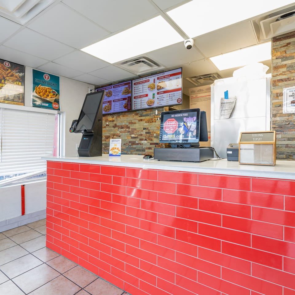 Bright fast-food counter with red tiled facade, digital menus displaying food, and POS systems.