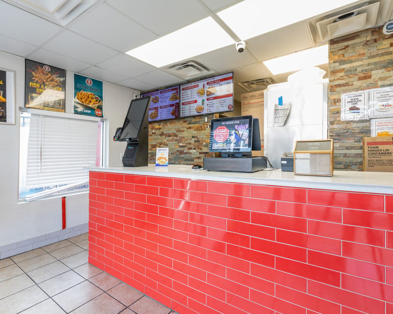 Bright fast-food counter with red tiled facade, digital menus displaying food, and POS systems.