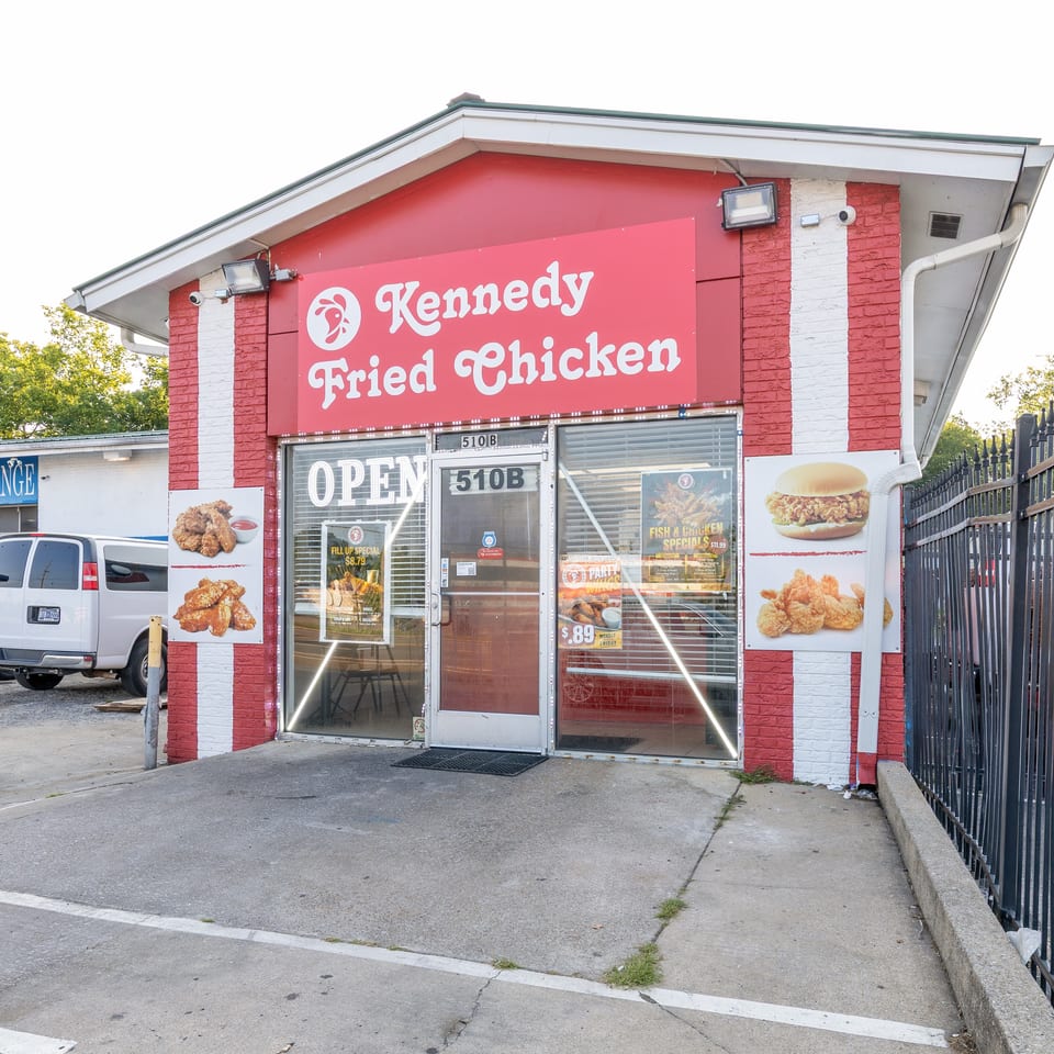 Exterior of Kennedy Fried Chicken restaurant with red and white stripes, "OPEN" sign, and food advertisements.