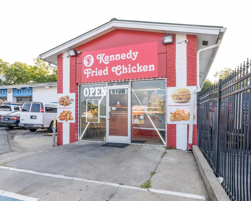 Exterior of Kennedy Fried Chicken restaurant with red and white stripes, "OPEN" sign, and food advertisements.