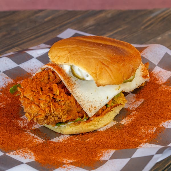 Spicy fried chicken sandwich with cheese and pickles on checkered paper.