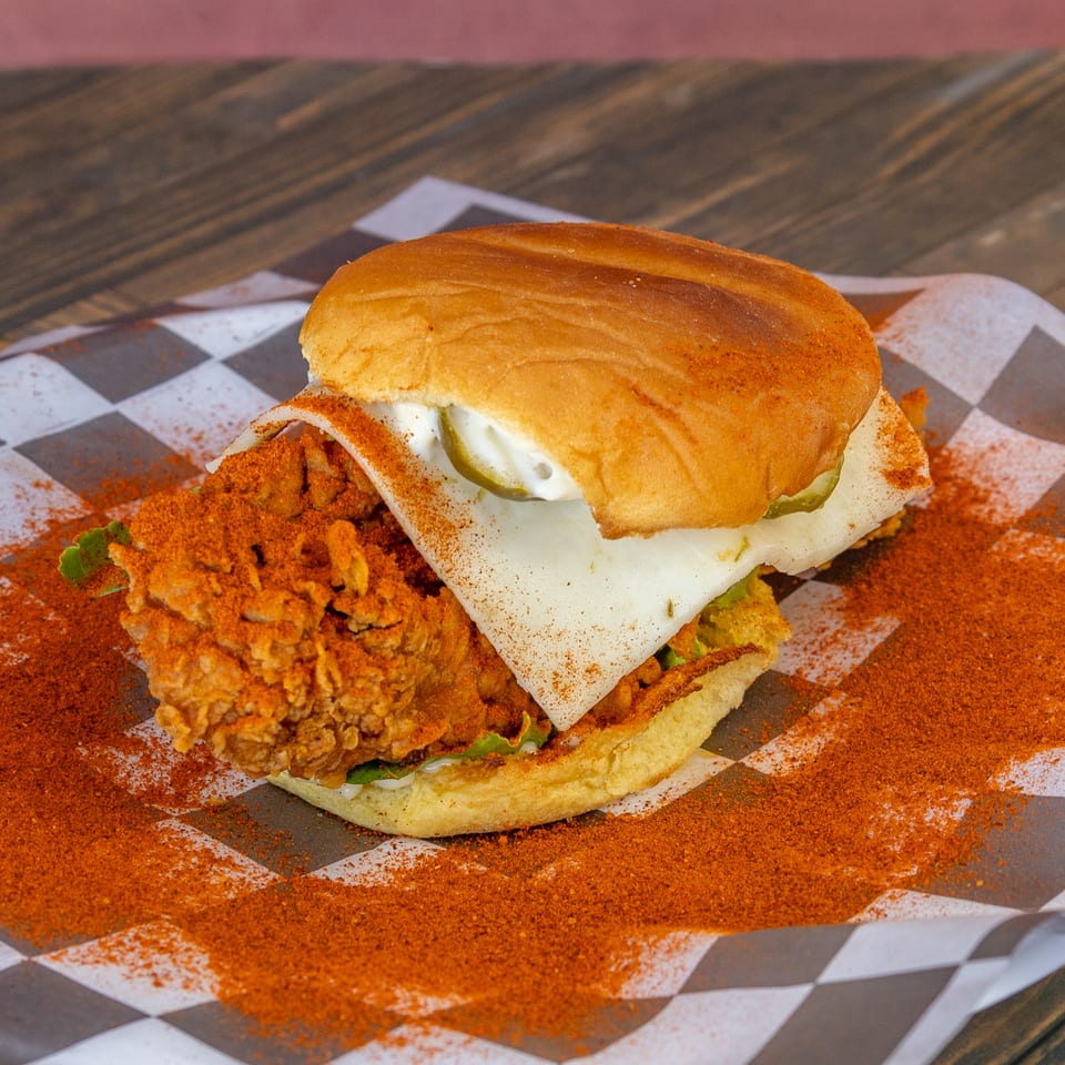 Spicy fried chicken sandwich with cheese and pickles on checkered paper.