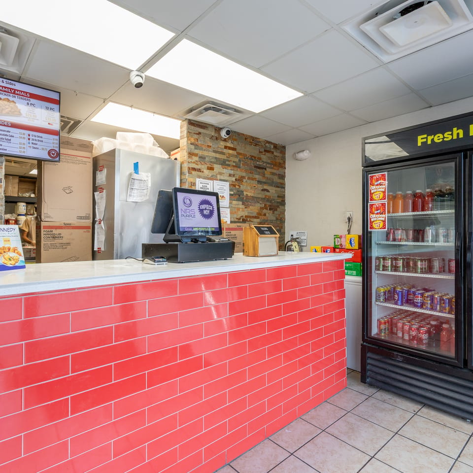 Restaurant counter with red tiled front, digital menu screen, and a "Fresh Food" beverage cooler.