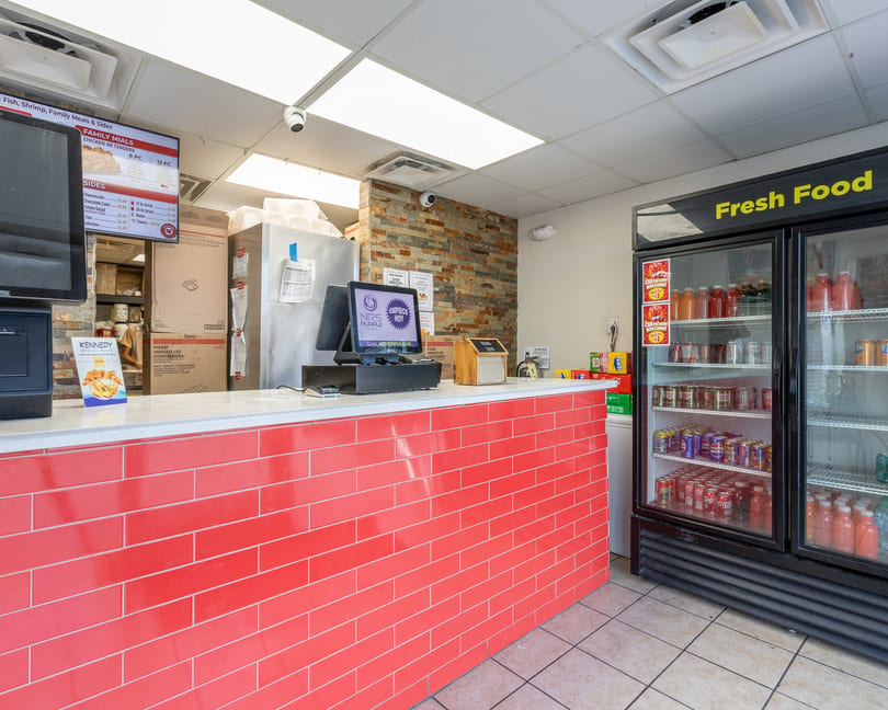 Restaurant counter with red tiled front, digital menu screen, and a "Fresh Food" beverage cooler.