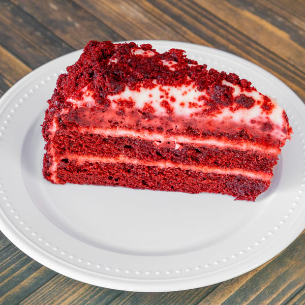 Slice of red velvet cake with cream cheese frosting on a white plate.