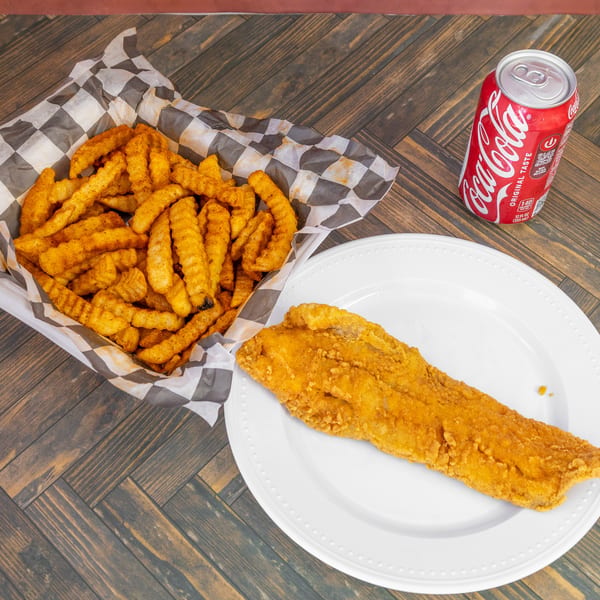 Fried fish fillet, seasoned crinkle-cut fries in a basket, and a Coca-Cola can on a wooden table.