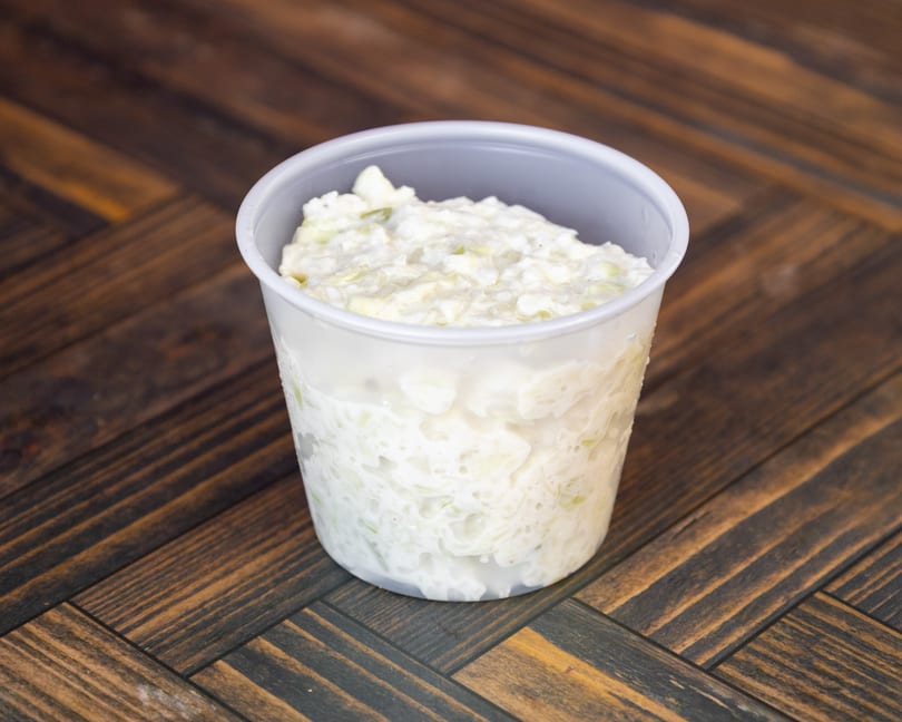 A serving of creamy coleslaw in a plastic cup on a dark wood surface.