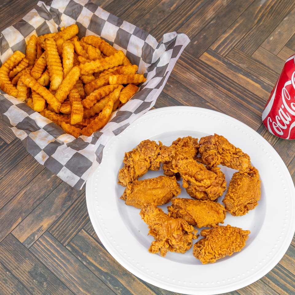 Seasoned crinkle-cut fries, fried chicken pieces, and a Coca-Cola can on a wooden table.