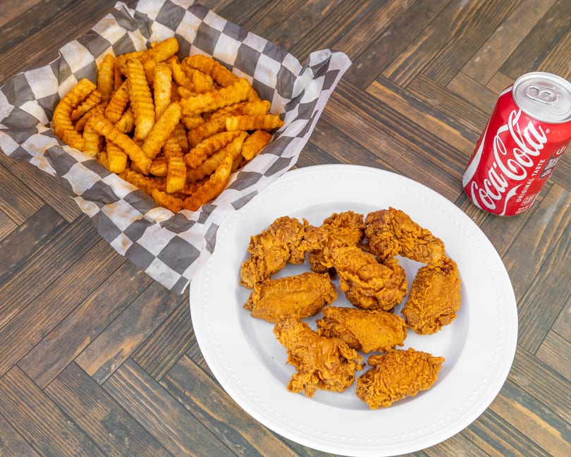 Seasoned crinkle-cut fries, fried chicken pieces, and a Coca-Cola can on a wooden table.