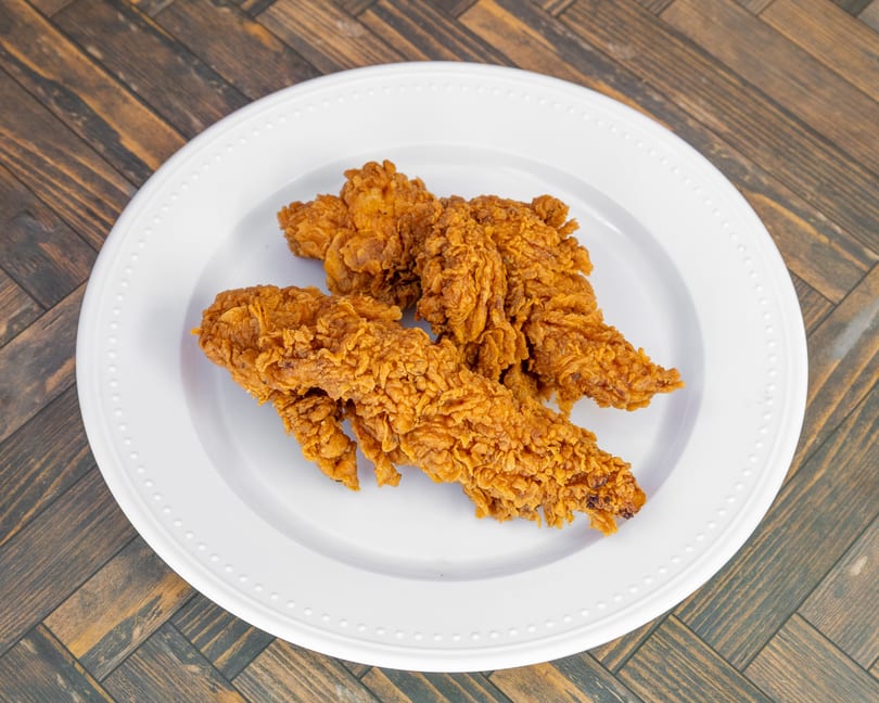 Golden-brown crispy fried chicken tenders on a white plate over a wooden table.
