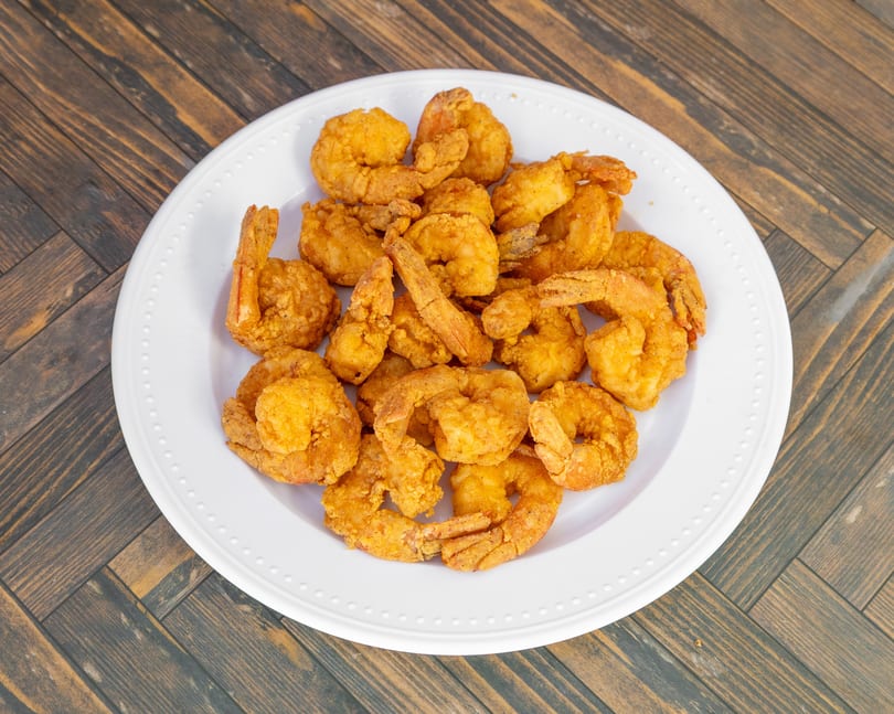 Golden fried shrimp piled on a white plate on a wooden table.