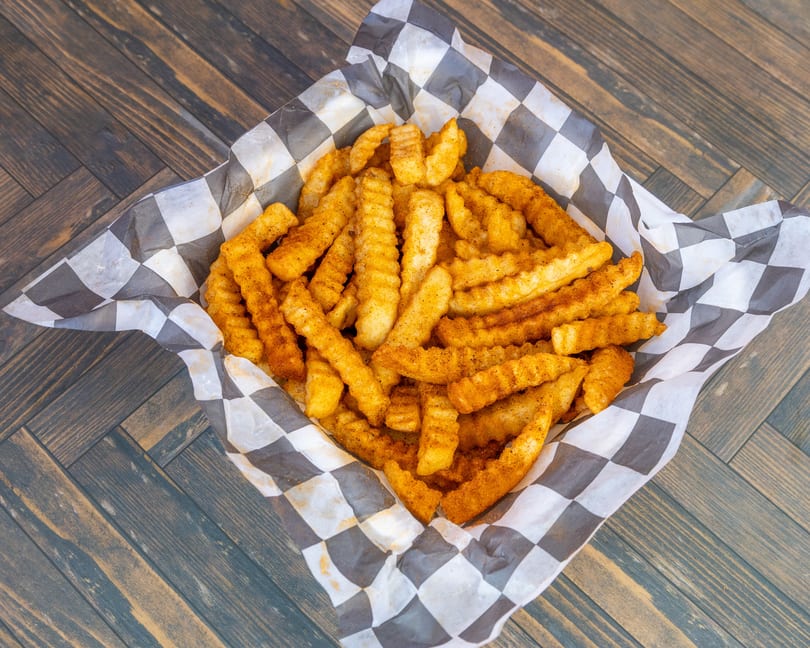 Golden crinkle-cut fries seasoned with spices in a checkered paper basket.