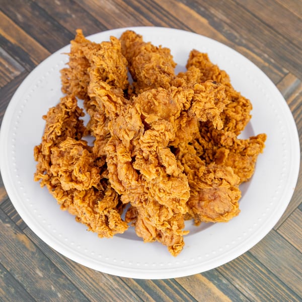 Crispy, golden-brown fried chicken pieces piled high on a white plate.