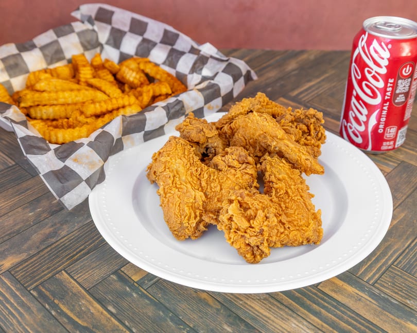 Golden fried chicken, crinkle fries in a basket, and a red Coca-Cola can.