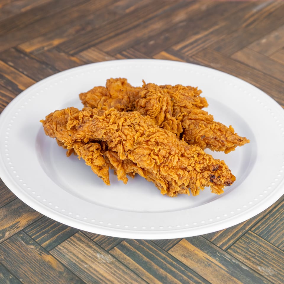Crispy golden brown fried chicken tenders on a white plate set on a wooden table.