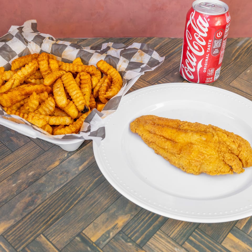 Fried fish fillet, seasoned crinkle-cut fries in a basket, and a Coca-Cola can on a wooden table.
