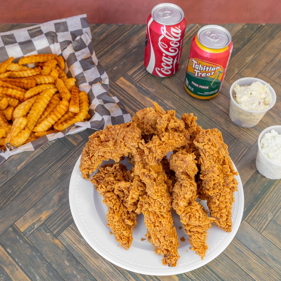 Fried chicken tenders, crinkle-cut fries, two sodas, and two side salads on a wooden table.