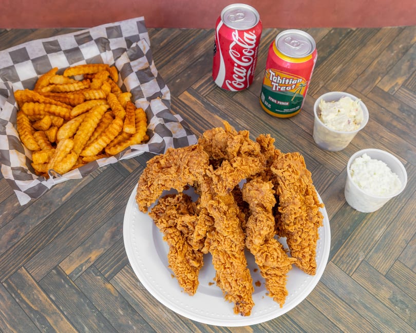 Fried chicken tenders, crinkle-cut fries, two sodas, and two side salads on a wooden table.