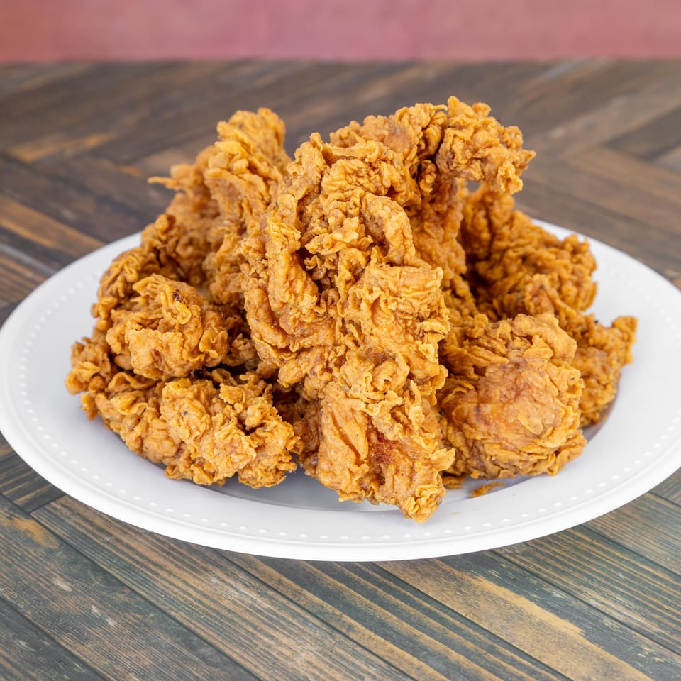Golden-brown crispy fried chicken pieces piled on a white plate atop a wooden table.