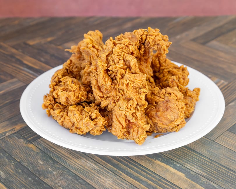Golden-brown crispy fried chicken pieces piled on a white plate atop a wooden table.