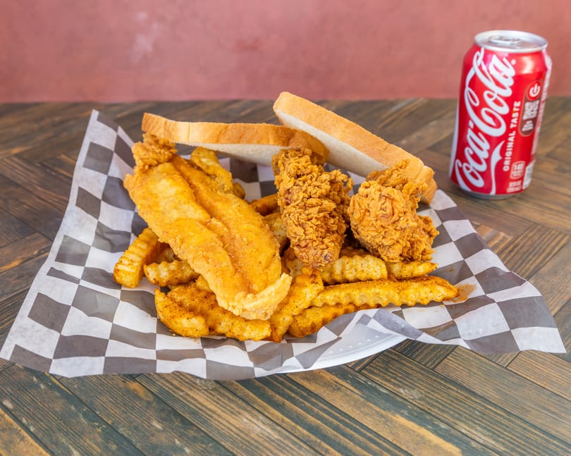 Golden fried fish, chicken, and seasoned fries with white bread and a Coca-Cola.