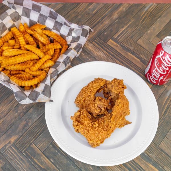 Fried chicken, crinkle-cut fries in a basket, and a Coca-Cola can on a wooden table.